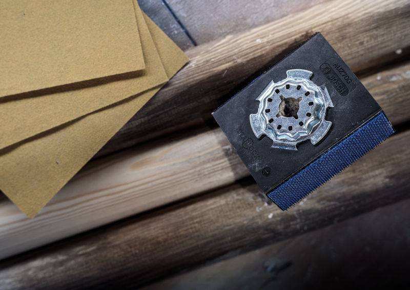 Schleifpapier und Schleifgerät auf Holzoberfläche, vorbereitet für eine handwerkliche Arbeit oder Restaurierung.