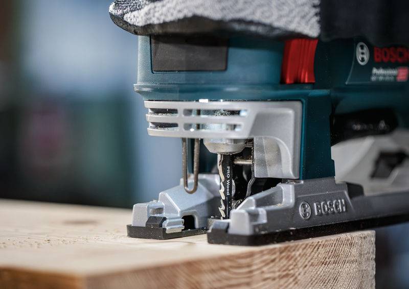 Eine elektrische Stichsäge schneidet durch ein Holzbrett. Die Nahaufnahme zeigt die Sägeblätter in Aktion und die Markenkennzeichnung.