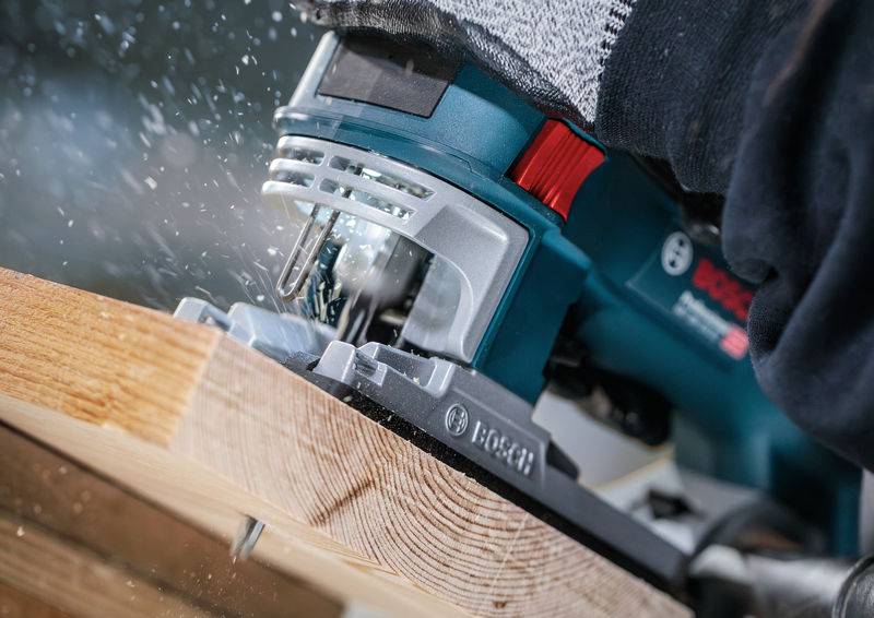 Eine Nahaufnahme zeigt eine Person, die eine elektrische Säge benutzt, um durch ein Holzstück zu schneiden. Späne fliegen bei der Arbeit.