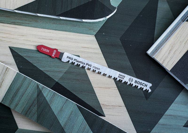 Ein Bosch-Sägeblatt liegt auf Holzbodenmuster. Es ist für 'PRO Plastics PVC clean' geeignet. Rotes Etikett mit '110mm' Längenangabe.