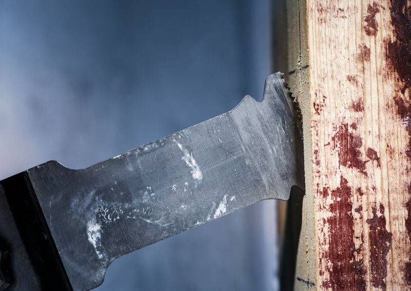 Nahaufnahme einer Säge, die durch ein Holzbrett schneidet, Holzspäne rundherum. Fokus auf die scharfe Klinge und ihre Bewegung.