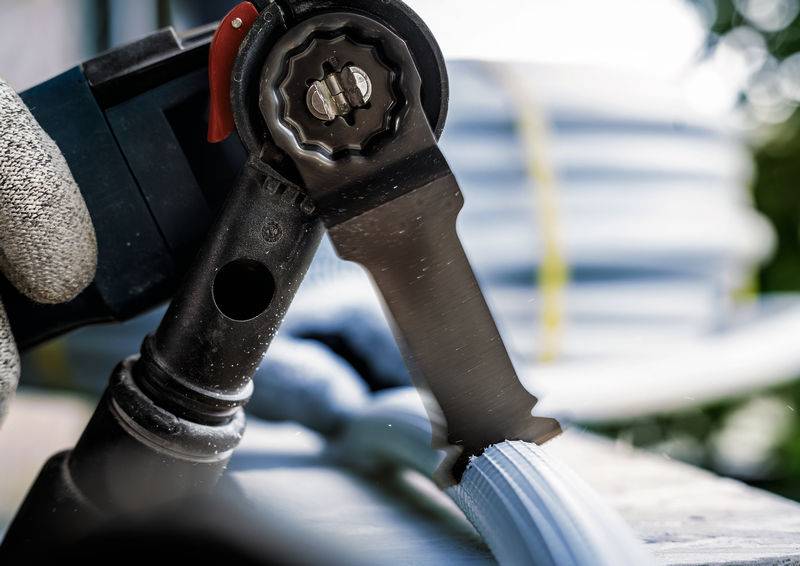 Nahaufnahme eines Kabelschneidwerkzeugs, das ein dickes Kabel durchtrennt. Eine Hand mit Schutzhandschuh hält das Werkzeug. Im Hintergrund sind weitere Kabel zu sehen.