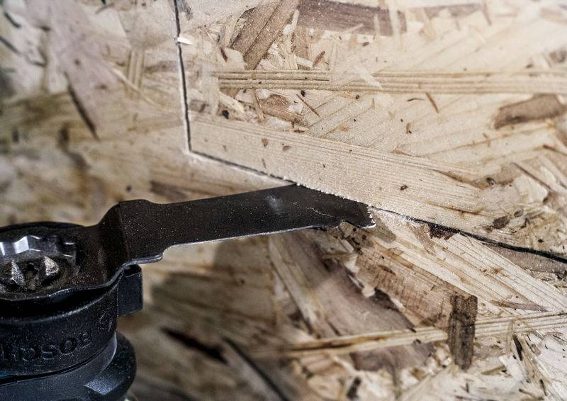 Ein oszillierendes Werkzeug schneidet eine gerade Linie in eine Spanplatte. Das Bild zeigt den präzisen Schnittvorgang.