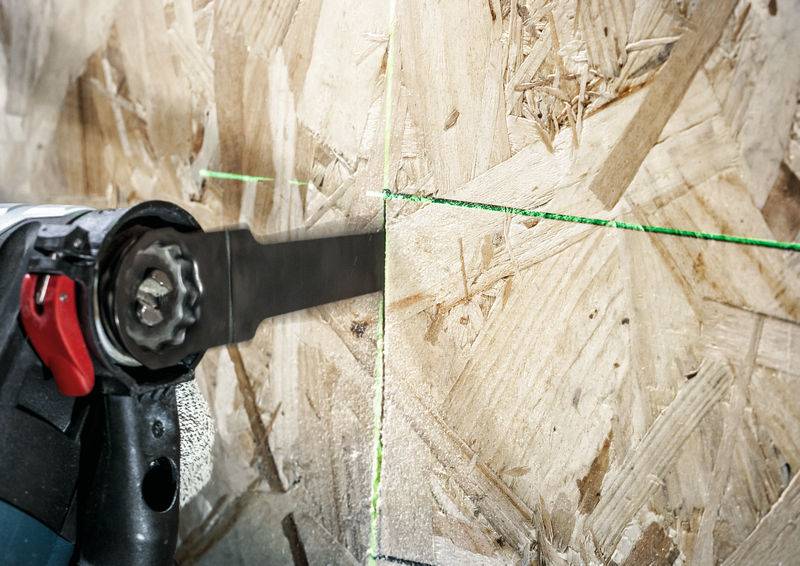 Ein Elektrowerkzeug mit Sägeblatt schneidet eine Holzplatte entlang einer grünen Laserlinie.