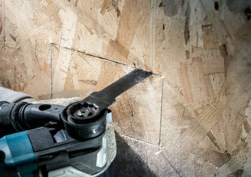 Eine elektrische Säge mit einem rechteckigen Sägeblatt schneidet ein quadratisches Loch in eine Holzplatte.