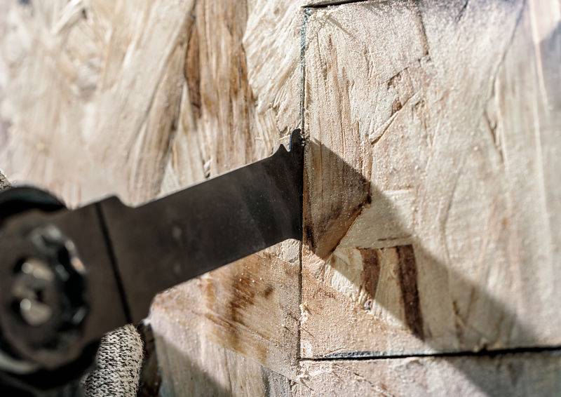 Ein elektrisches Sägeblatt schneidet durch eine Holzplatte, vermutlich Spanplatte. Das Bild zeigt den Schnittvorgang aus nächster Nähe.