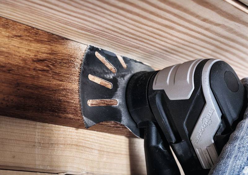 Eine elektrische Schleifmaschine wird auf einem Holzbrett verwendet. Das Schleifpapier glättet die Holzoberfläche.