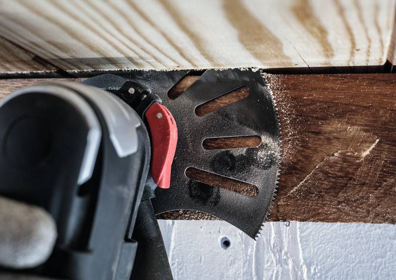 Ein Multifunktionswerkzeug mit einer Sägeklinge schneidet durch ein Holzbrett, das an einem Rahmen befestigt ist.