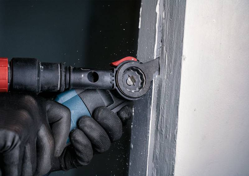 Hand hält ein oszillierendes Werkzeug, schneidet ein Stück Holz an einem Türrahmen. Arbeiter trägt schwarze Handschuhe für Sicherheit.