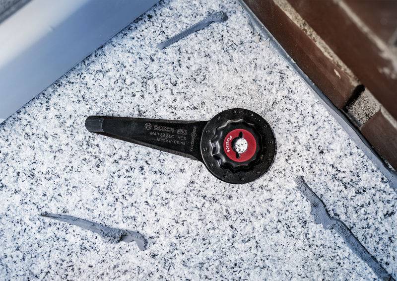 Ein schwarzer Schraubenschlüssel mit rotem Drehknopf liegt auf einer mit Schnee bedeckten Oberfläche neben einer Mauer.