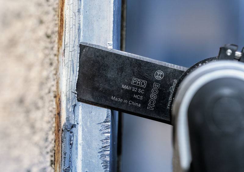 Handwerkzeug schneidet Dichtungsmasse an einem Fensterrahmen. Die Klinge trägt die Aufschrift 'Bosch'. Nahaufnahme.