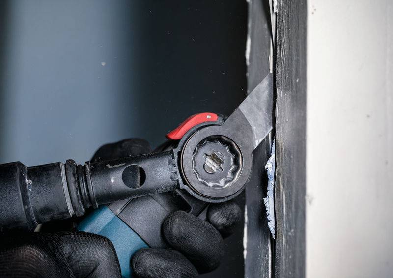 Eine Person arbeitet mit einem elektrischen Werkzeug, um Material von einer Kante zu entfernen. Die Handschuhe schützen die Hände.