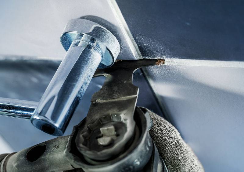 Nahaufnahme eines Winkelschleifers, der Fliesenfugen bearbeitet. Die Handwerkerhand trägt einen Handschuh. Fliesen in Blau- und Grautönen.