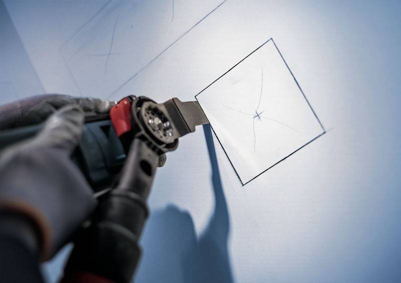 Eine Person schneidet präzise ein quadratisches Loch in eine Wand mit einem elektrischen Werkzeug, möglicherweise für eine Installation.