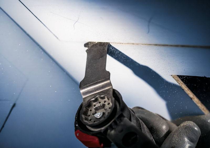 Eine Nahaufnahme einer elektrischen Säge, die ein Stück Material durchtrennt. Die grauen Handschuhe des Benutzers sind teilweise sichtbar.