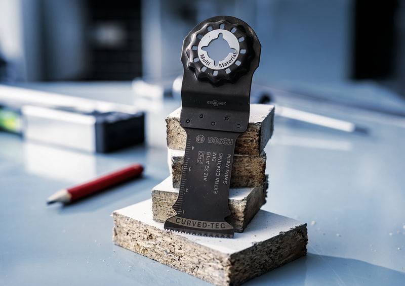 Multifunktionswerkzeug-Sägeblatt auf gestapelten Holzstücken, mit einem Schraubenschlüssel in der Nähe auf einem Metalltisch.