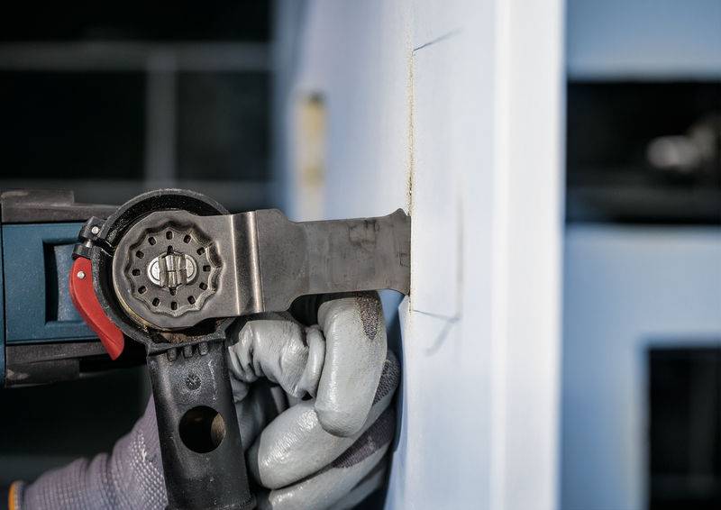 Person schneidet rechteckige Öffnung in eine Wand mit oszillierendem Multifunktionswerkzeug. Werkzeug hat Metallsägeblatt.