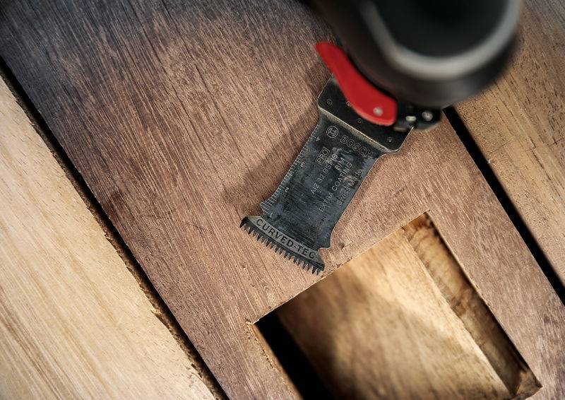 Ein Multitool mit Sägeblatt schneidet präzise ein quadratisches Loch in Holz. Die Aufnahme zeigt das Werkzeug in Aktion.