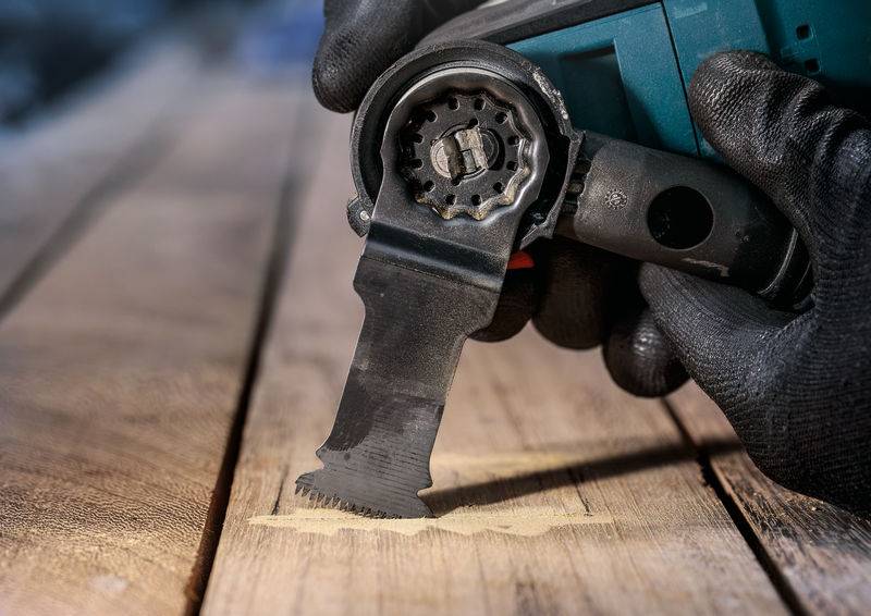 Eine Person verwendet ein elektrisches Multitool mit Sägeaufsatz, um ein präzises Stück Holz auf einer Werkbank zu schneiden.