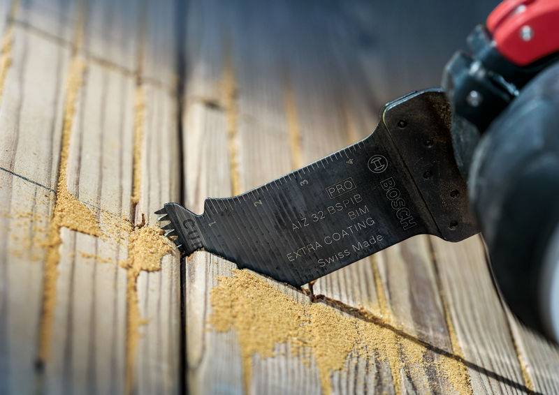 Ein Multifunktionswerkzeug mit Sägeaufsatz schneidet Holz. Holzspäne umgeben die Klinge, die in einem Holzbrettritzen steckt.