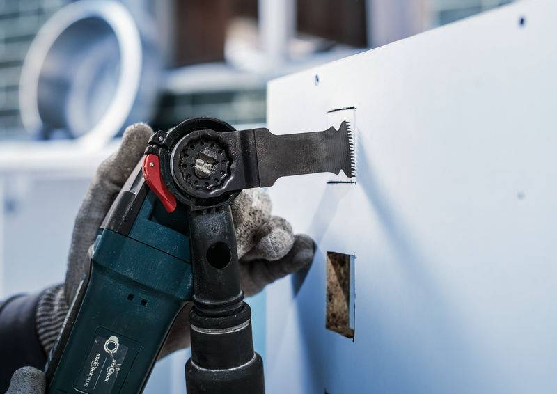 Eine Person schneidet mit einem elektrischen Werkzeug ein rechteckiges Loch in eine Wand. Nahaufnahme des Werkzeugs beim Schneidevorgang.