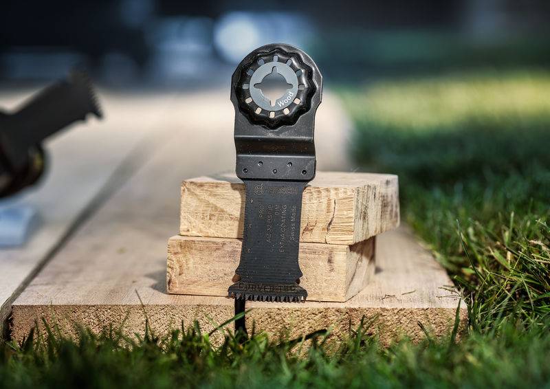 Eine Multitool-Klinge steht auf gestapelten Holzbrettern im Freien. Sie ist für Feinarbeiten in Holz und Nägeln konzipiert.