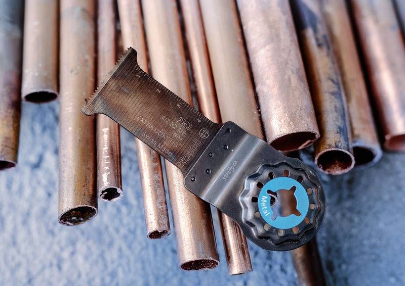 Verschlissene Kupferrohre liegen auf einem Tisch, ein Schneidwerkzeug mit blauem Emblem ruht darauf, bereit zum Einsatz.