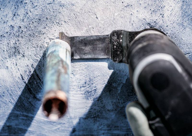 Eine Nahaufnahme eines Elektrowerkzeugs, das ein Metallrohr schneidet. Der Hintergrund ist unscharf und das Werkzeug wird von einer Person gehalten.