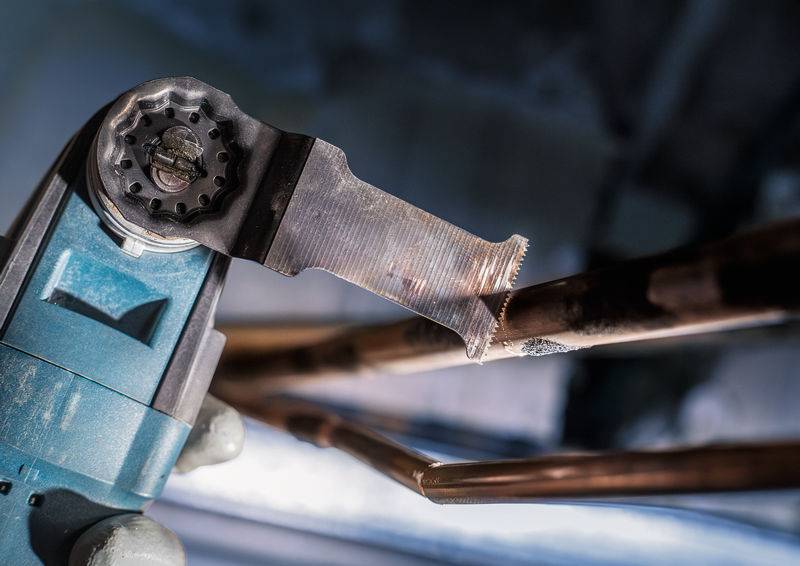 Eine Maschine schneidet Kupferrohre in einem industriellen Umfeld. Die Rohre verlaufen horizontal und die Maschine hat eine Metallsäge.