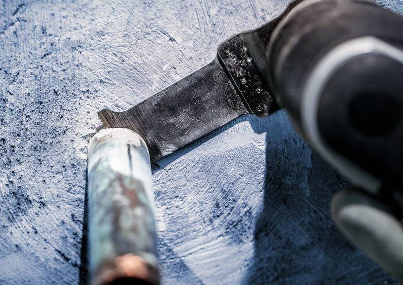 Nahaufnahme eines Schneidwerkzeugs, das ein Metallrohr abschneidet. Grobe blaue Oberfläche im Hintergrund.