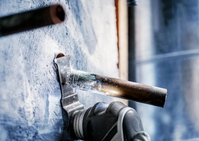 Ein Installateur lötet ein Kupferrohr an einer Wandverbindung. Funken fliegen umher, während das Metall erhitzt wird.