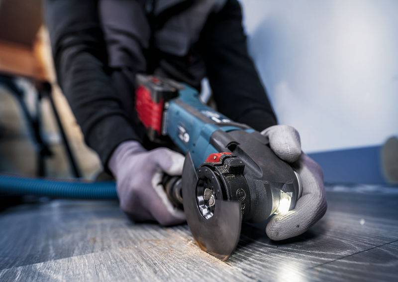 Eine Person schneidet mit einem Winkelschleifer einen Bodenbelag. Trägt Arbeitshandschuhe und Schutzkleidung.