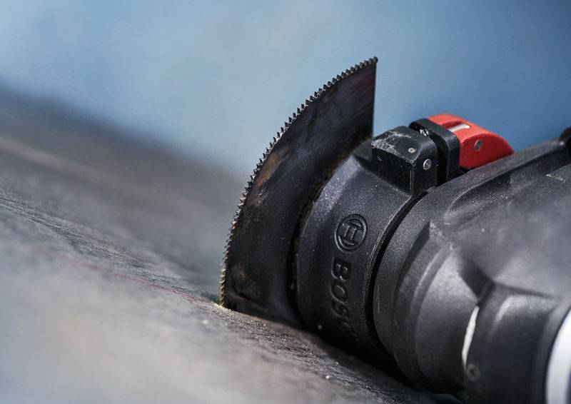 Nahaufnahme eines elektrischen Werkzeugs mit Sägeaufsatz, das präzise in eine dunkle Oberfläche schneidet.