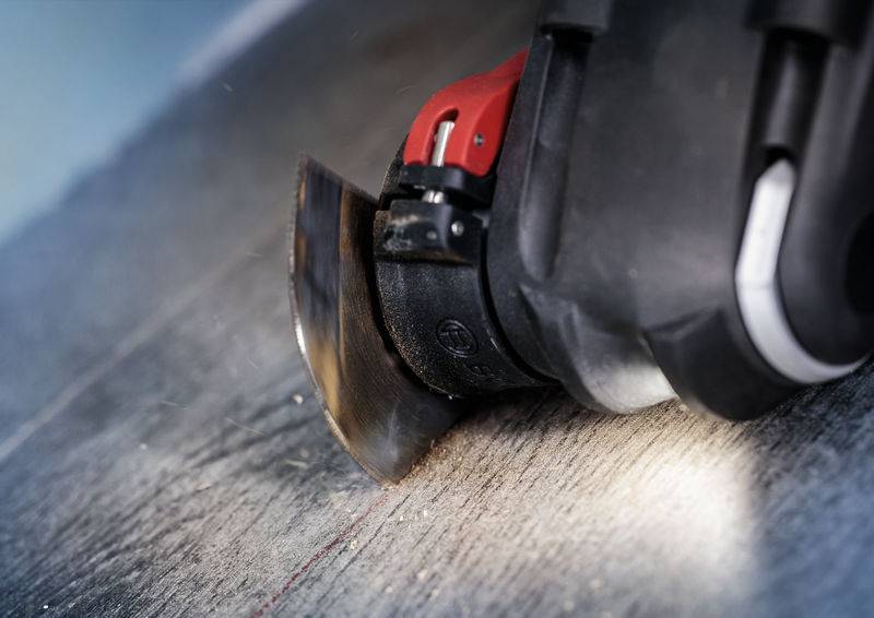 Nahaufnahme eines oszillierenden Werkzeugs mit rotierendem Sägeblatt, das eine gerade Linie in einen Holzuntergrund schneidet.