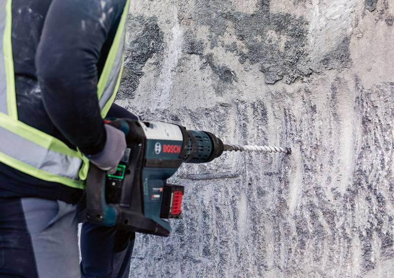 Eine Person bohrt mit einer Bohrmaschine in eine Betonwand. Sie trägt Sicherheitskleidung.