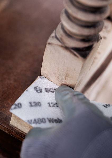 Person schleift Holzmöbel mit Schleifpapier, um Oberfläche zu glätten. Nahaufnahme zeigt Hand in Handschuh, Fokus auf Material und Objektkante.