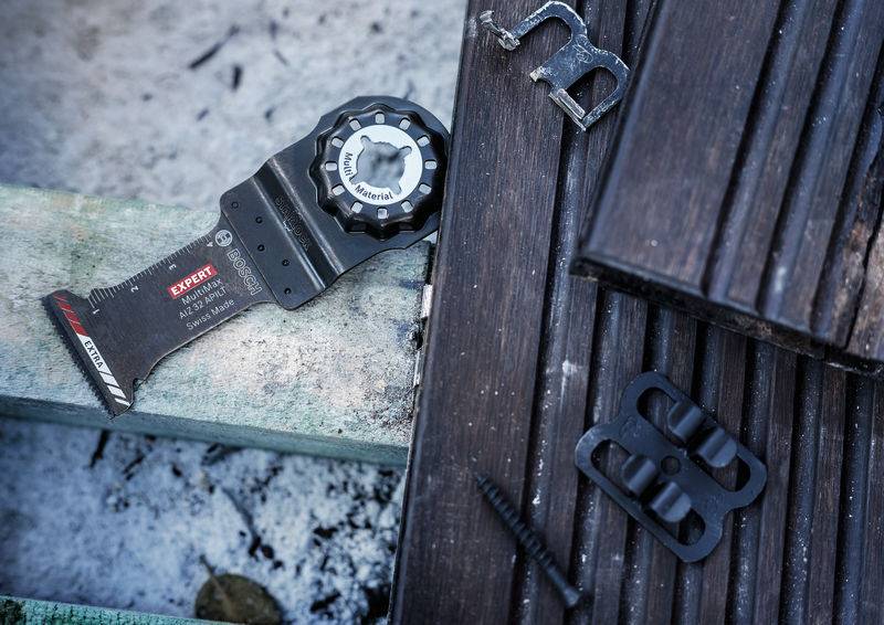 Ein Multifunktionswerkzeug mit Sägeblatt liegt auf Holzbrettern, umgeben von Schrauben und Metallstücken, bereit für Handwerksarbeiten.