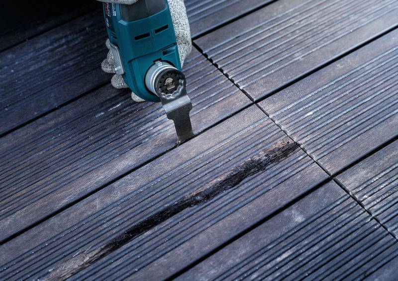 Ein Elektrowerkzeug mit oszillierender Klinge schneidet präzise durch eine beschädigte Diele eines Holzdecks, um es zu reparieren.