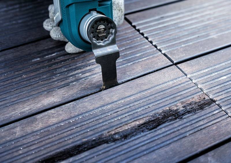 Ein oszillierendes Werkzeug schneidet präzise in eine Holzterrasse, um Anpassungen oder Reparaturen vorzunehmen.