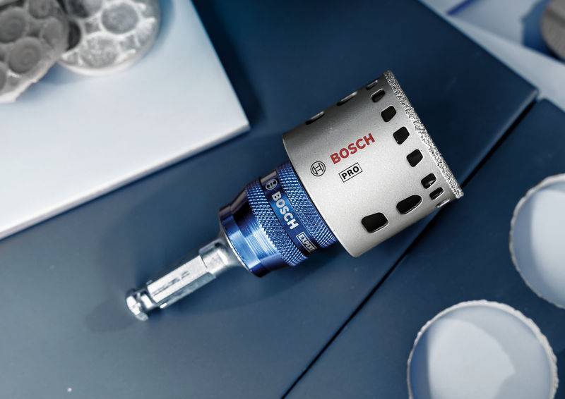 Ein Bosch Pro Lochsägen-Aufsatz liegt auf einem Tisch. Links sind Bohrlöcher zu sehen. Das Bild zeigt Werkzeug für handwerkliche Arbeiten.