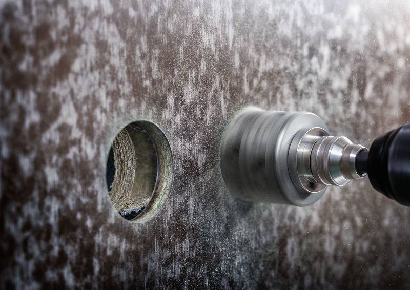 Eine Bohrmaschine mit einem runden Bohrer bohrt ein Loch in eine Metallplatte neben einem bereits bestehenden Loch.