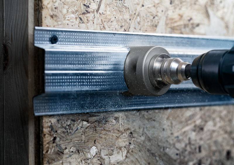 Ein Bohraufsatz dreht sich auf einer Metallstrebe, die an einer Spanplatte befestigt ist. Es entstehen Metallspäne.