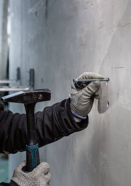Hand in Arbeitshandschuh hält Hammer und Meißel, um in Betonwand zu meißeln.