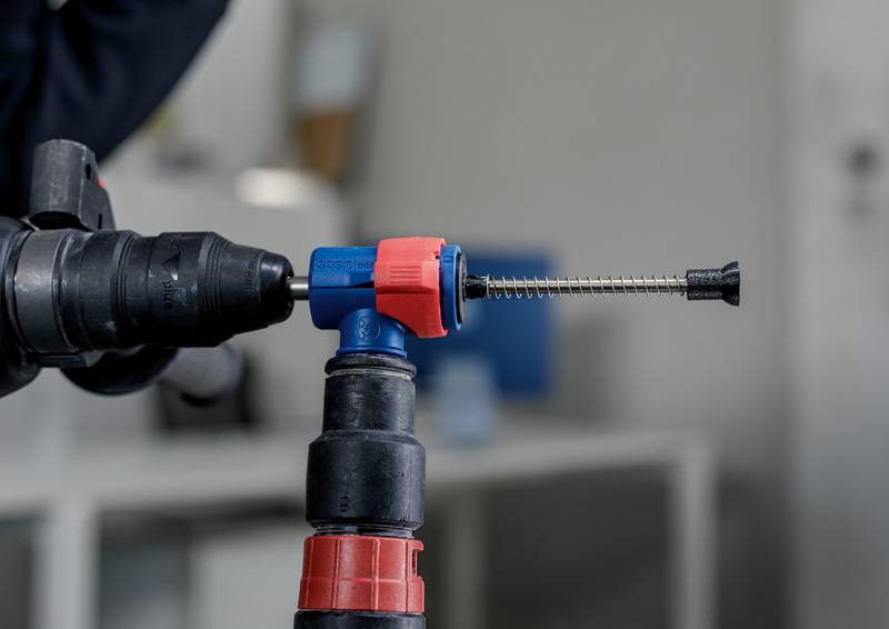 Nahaufnahme eines Bohrers mit einem Spezialaufsatz für präzise Metallarbeiten, fokussiert auf die Spitze. Im Hintergrund unscharfe Werkstattumgebung.