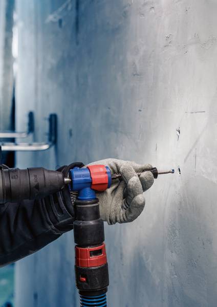 Eine Hand mit Handschuh hält einen Bohrer, der in eine Betonwand gebohrt wird.