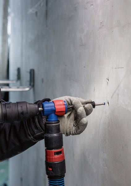 Eine Person bohrt mit einem Bohrhammer ein Loch in eine Betonwand. Der Bohrer wird mit beiden Händen gehalten und trägt Handschuhe.