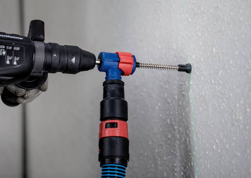 Ein Arbeiter benutzt einen Bohrhammer, um eine Schraube in eine Wand zu befestigen. Ein grüner Lasernivellierer ist auf der Wand sichtbar.