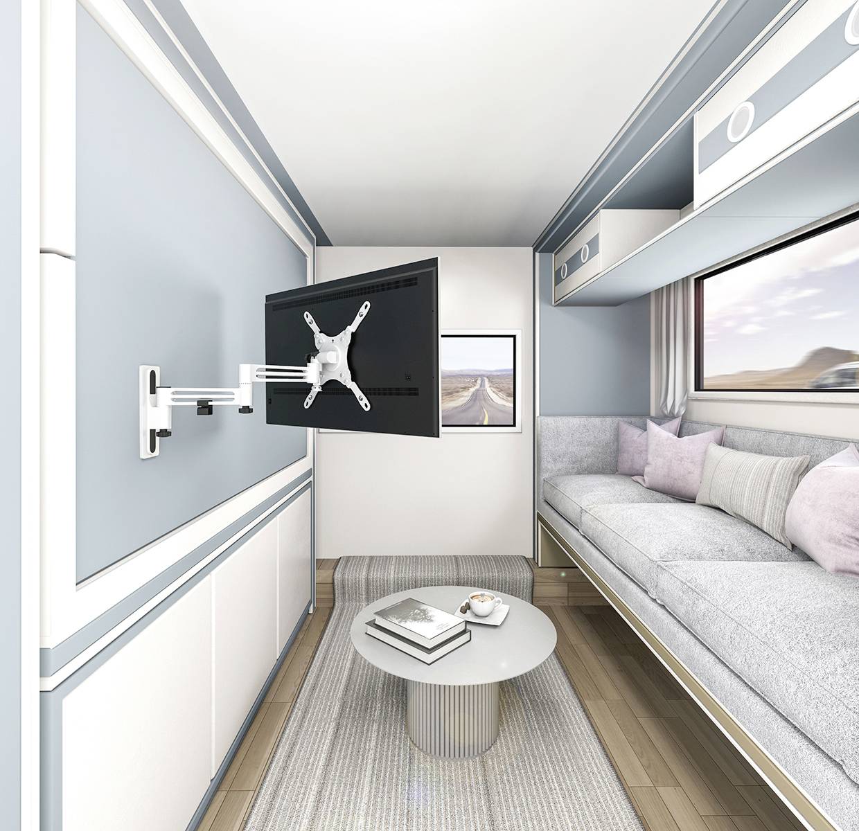 Ein moderner, kleiner Wohnraum mit einem grauen Sofa, einem runden Couchtisch und einem an der Wand montierten Fernseher. Fenster mit Wüstenblick.