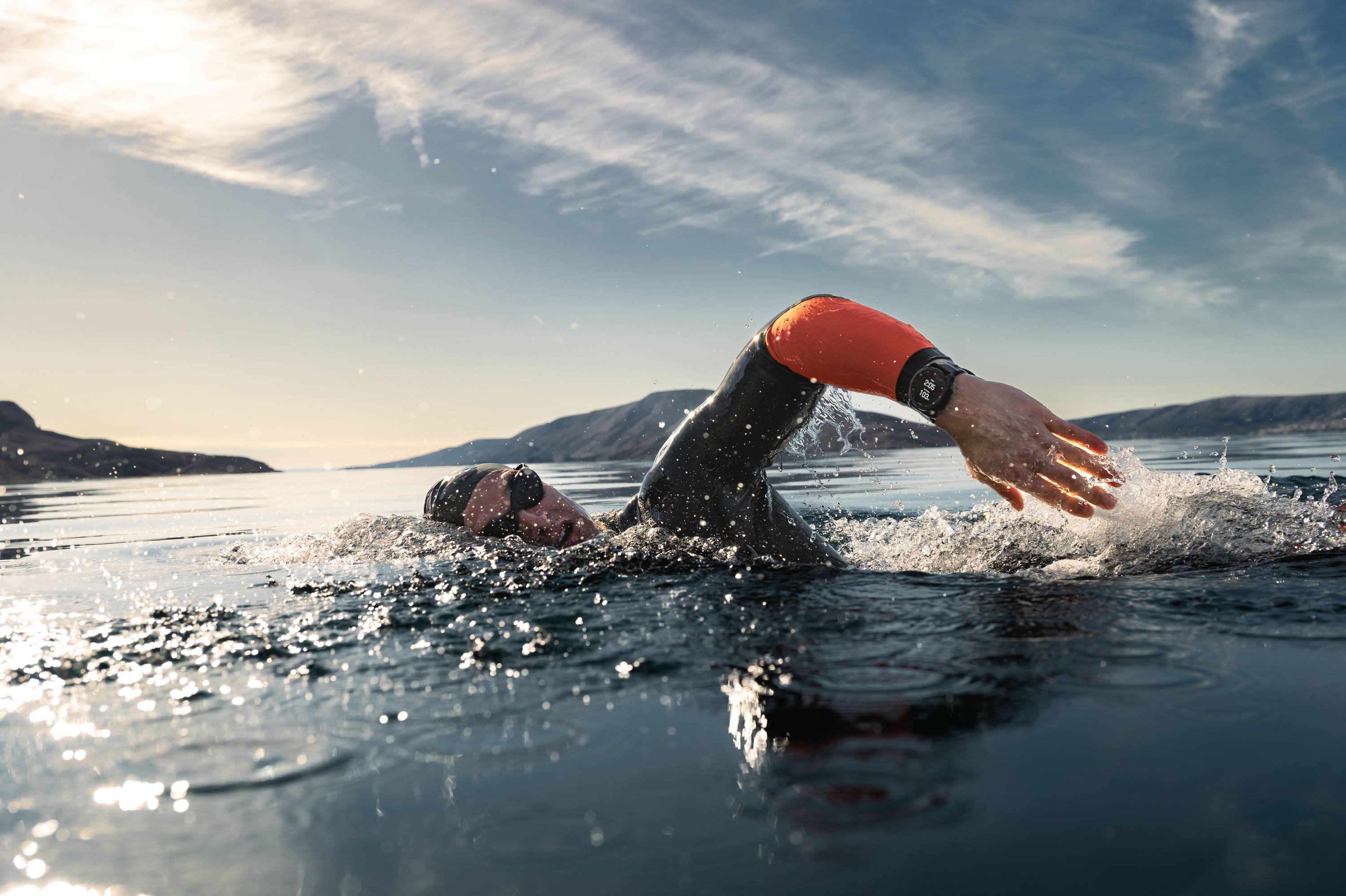 Eine Person schwimmt in einem Neoprenanzug in einem ruhigen Gewässer, umgeben von Bergen und einem klaren Himmel.