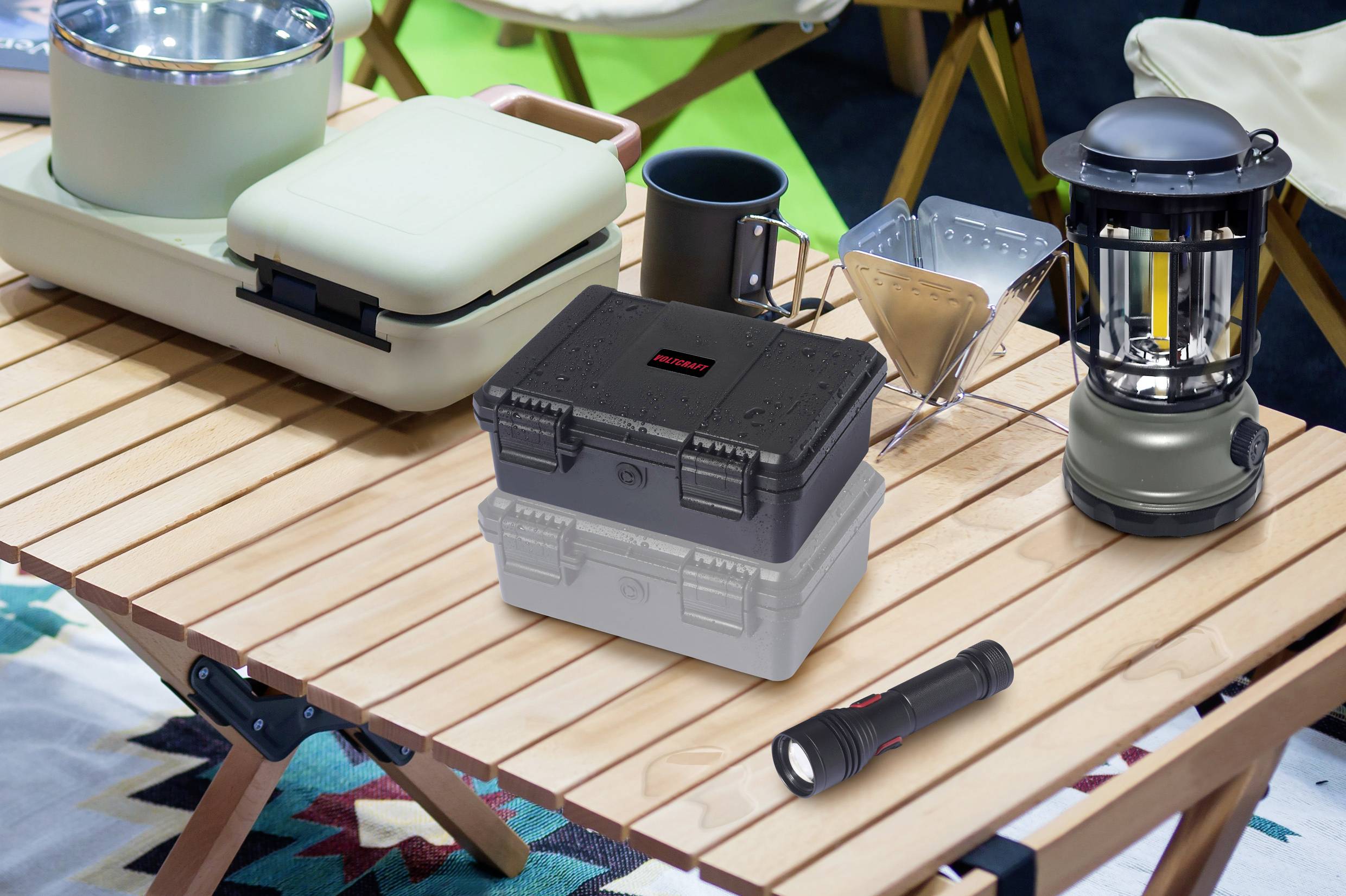 Ein Campingtisch mit Kaffeekocher, Taschenlampe, Laterne, Geschirr und zwei stapelbaren Aufbewahrungsboxen.